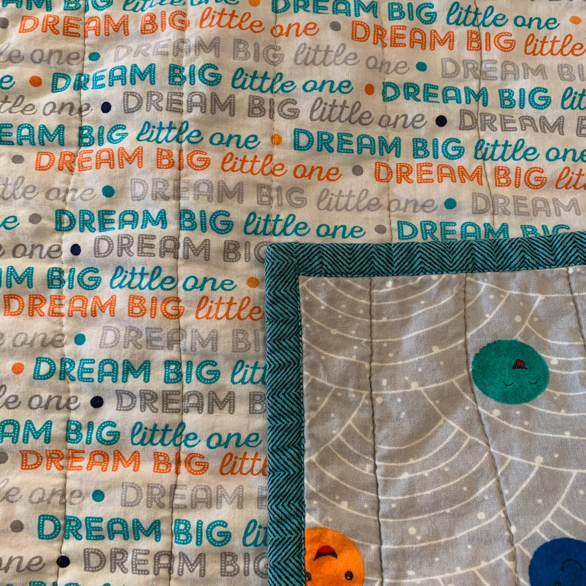 Close-up of teal binding, planet print, and Dream Big backing on cotton baby quilt