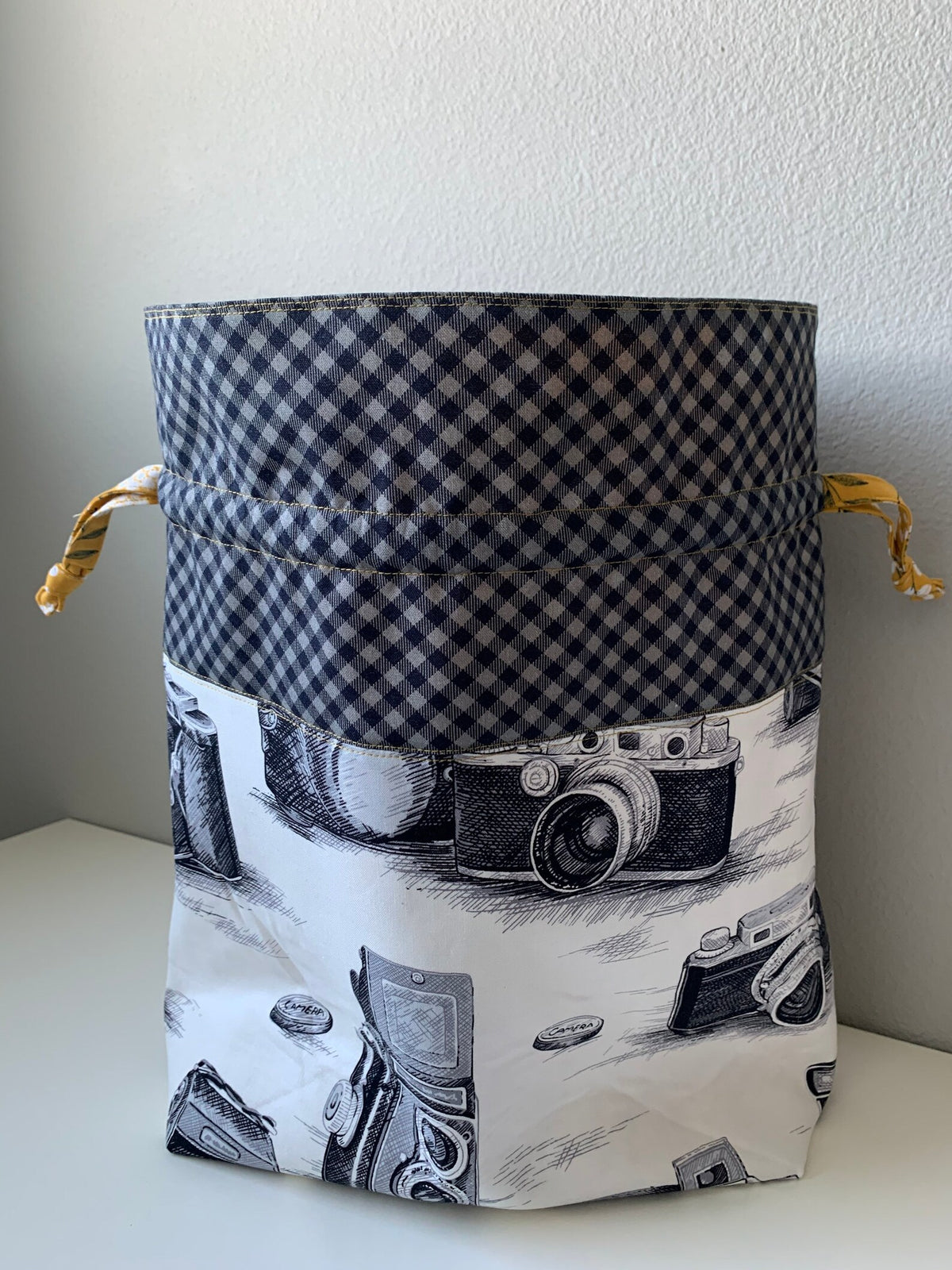 Open lined drawstring bag showing camera print body and dark checked upper panel