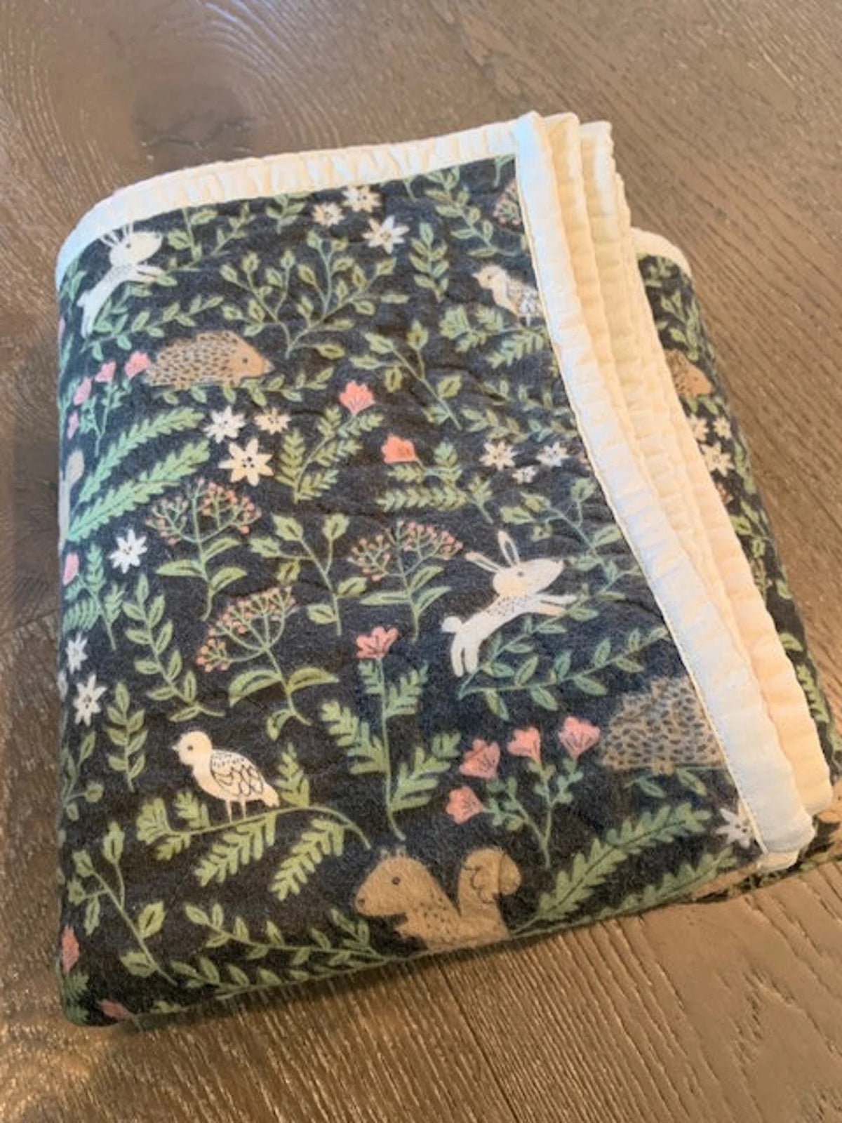 Folded woodland flannel baby quilt with forest animals and cream-colored binding