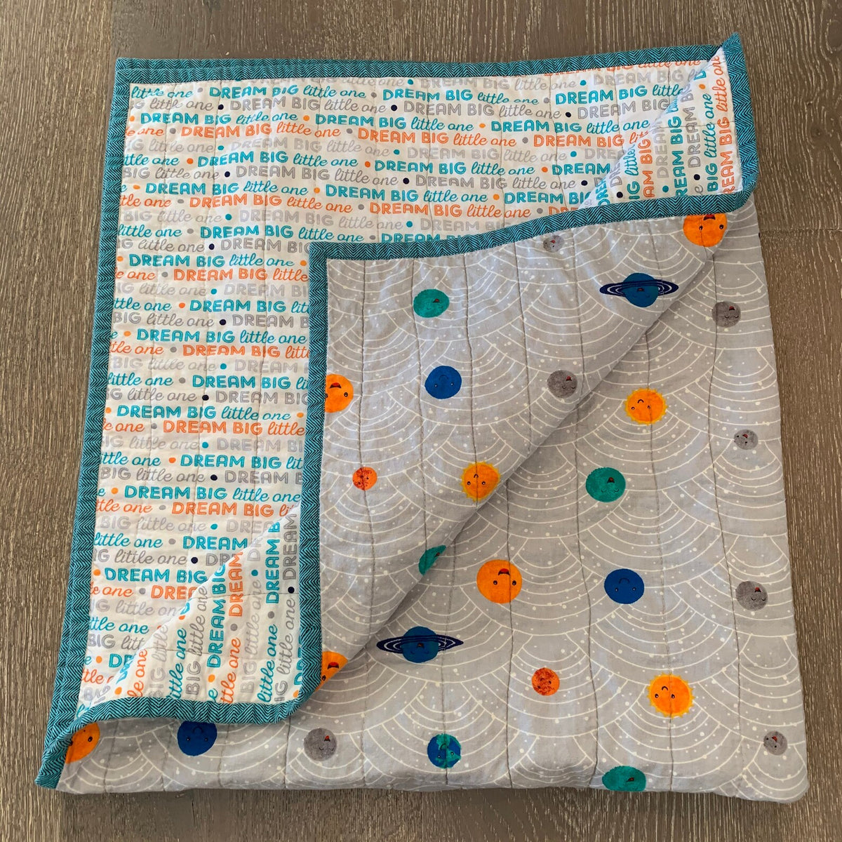 Folded planets baby quilt showing gray planet print and coordinating Dream Big backing