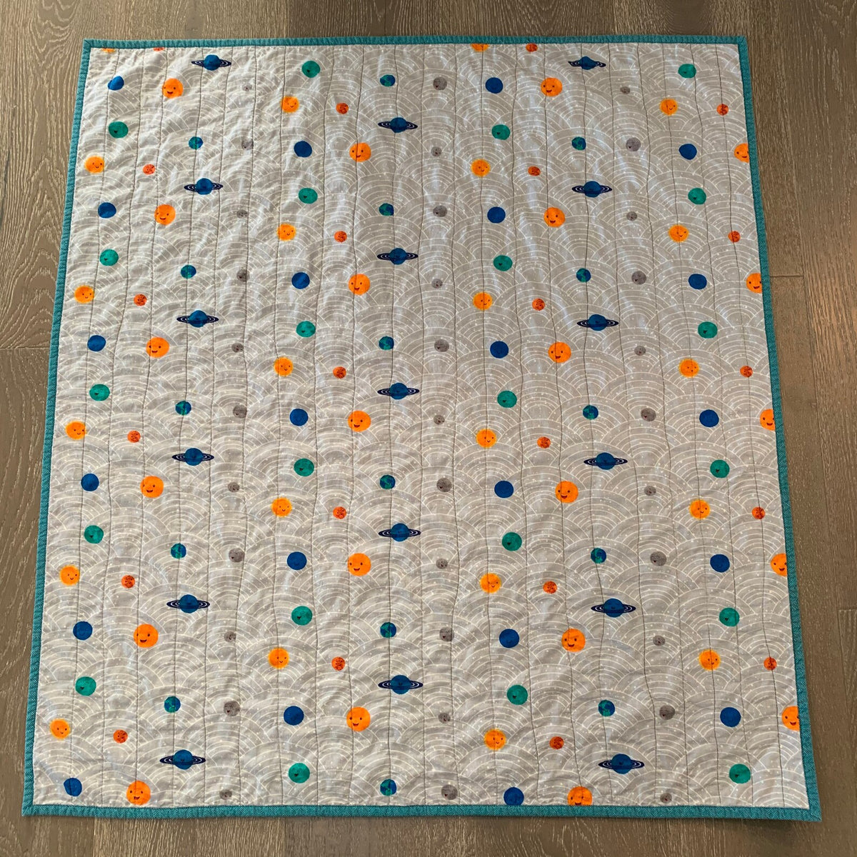 Handmade planets baby quilt with teal binding and colorful planets on a gray background