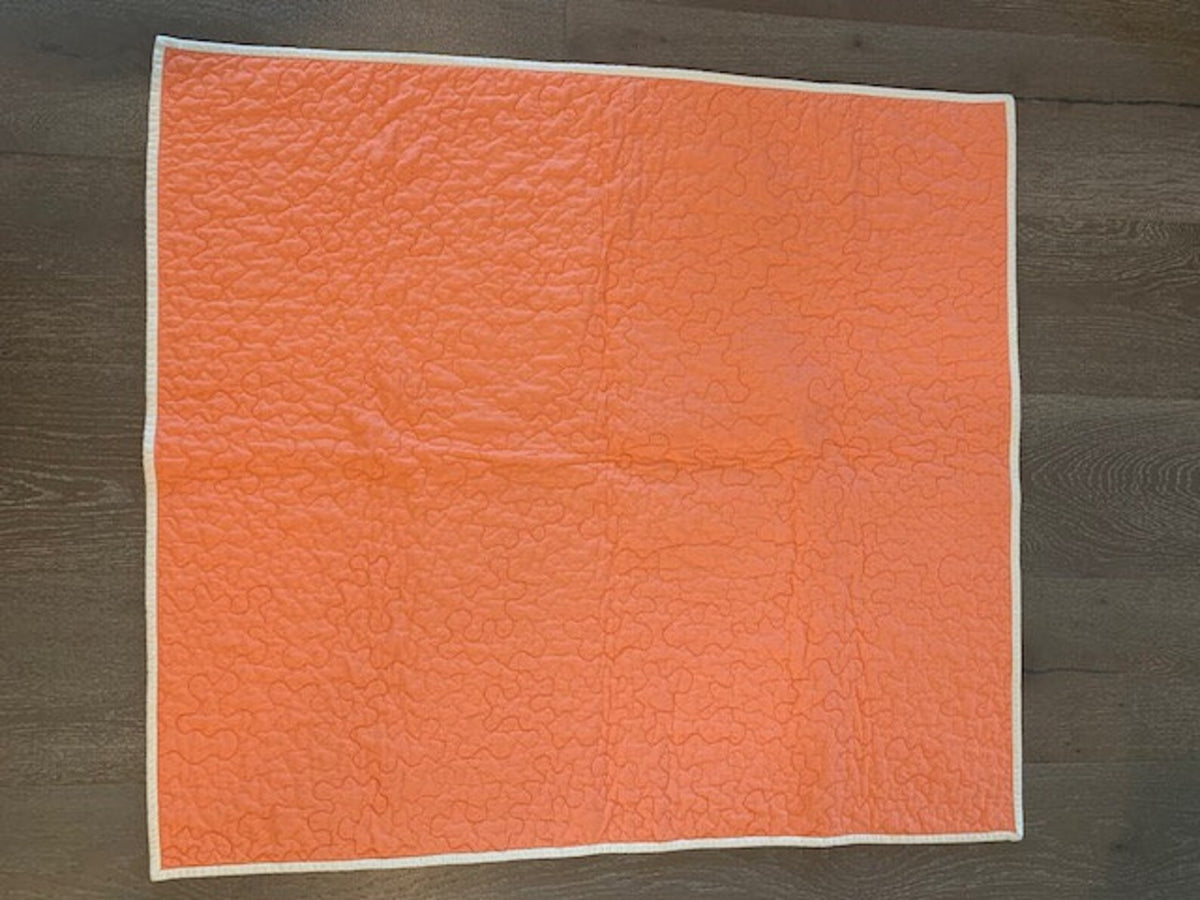 Peach-coral backing of handmade baby quilt showing free-motion stipple quilting